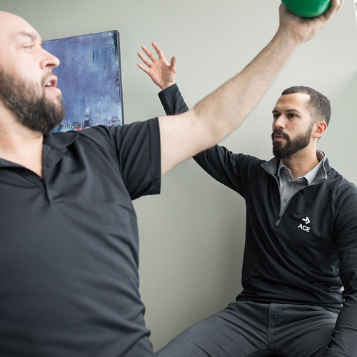 a medical exercise specialist working with a patient to lift their arms above their head